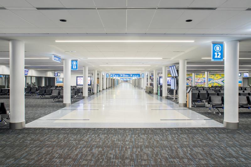 complete image of Concourse B terminal renovations, long hallway with carpeted area and seating by each gate, terminal signage and digital boards   
