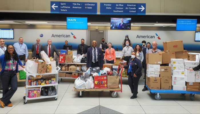CLT Airport employees and airline employees gathered in front of American Airlines ticketing counter, employees are smiling big standing near carts with boxes of non-perishable and essential items for a giveaway 