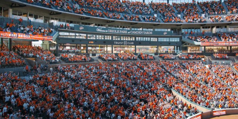Crowd of fans fills the stands at Oriole Park at Camden Yards during a baseball game, with the Truist Club visible above the seating.